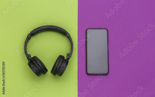 Wireless stereo headphones and smartphone on green purple background. Top view