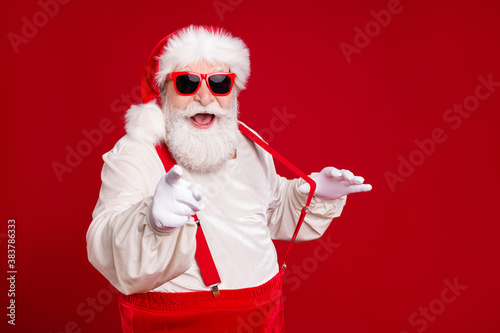 Close-up portrait of his he nice handsome cheerful cheery excited bearded fat Santa pulling suspenders pointing at you having fun invite date isolated bright vivid shine vibrant red color background