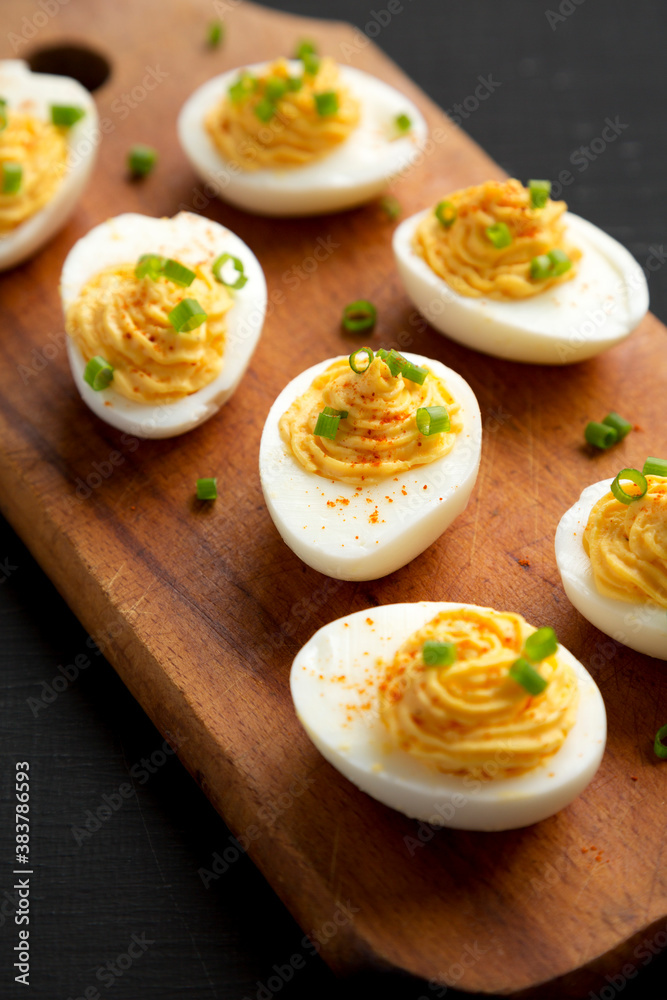 Homemade Deviled Eggs with Chives on a rustic wooden board on a black background, side view. Close-up.