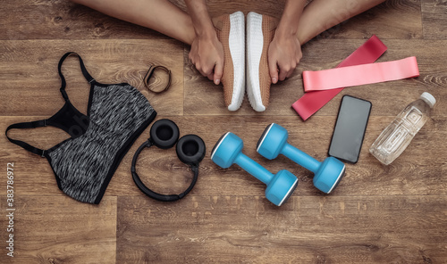 Flat lay composition of woman legs, sports equipment and clothes on a wooden floor. Fitness, sport and healthy lifestyle concept. Top view