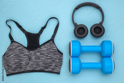 Sports top bra, dumbbells and stereo headphones on blue background. Sport and fitness. Top view. Flat lay
