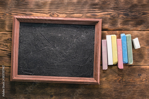 Colorful chalks and blackboard on the brown wooden desk background. photo