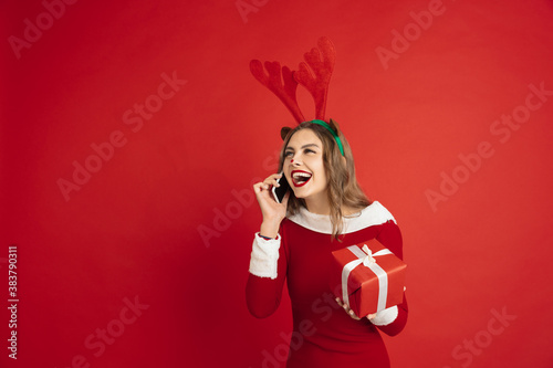Talking phone with gift. Concept of Christmas, 2021 New Year's, winter mood, holidays. Copyspace for ad, postcard. Beautiful caucasian woman with long hair like Santa's Reindeer catching giftbox.