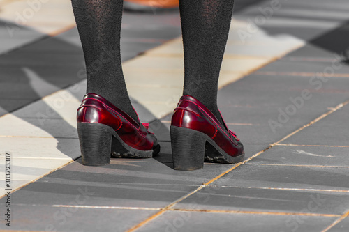 Halloween themes, dressing up for party. Closeup shot of new shiny red shoes with heel. Young woman standing on the street, black stockings, natural sunset light, warm october afternoon.