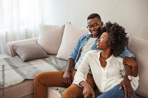 Shot of a couple resting on the couch watching television. Young loving couple communicating while relaxing on sofa and watching a TV at home.