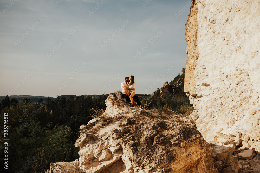 Young couple in love together in summer trip in the mountain. Romantic couple of pretty girl and handsome man in love kiss on cliff on summer day over mountain tops. Copy space.