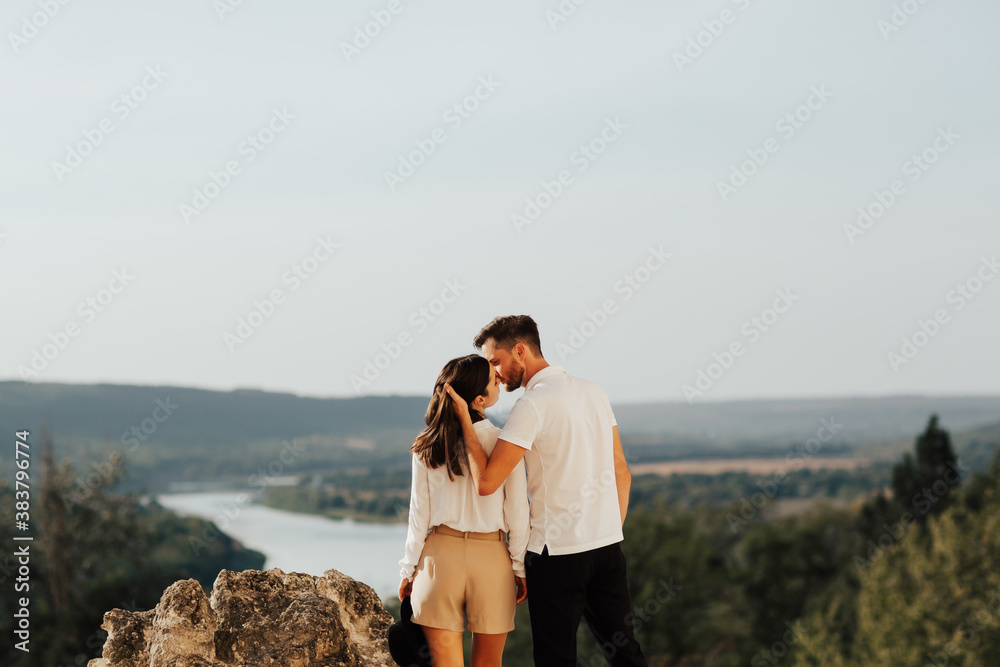 A couple hugging and kissing on the top of the mountain. They standing with their backs to the camera. Copy space.
