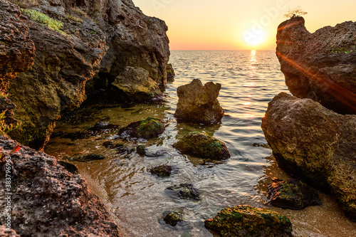 Huge stones and rock near the sea. Sea water washes the stones at sunset. The sun's rays shine through the stones.