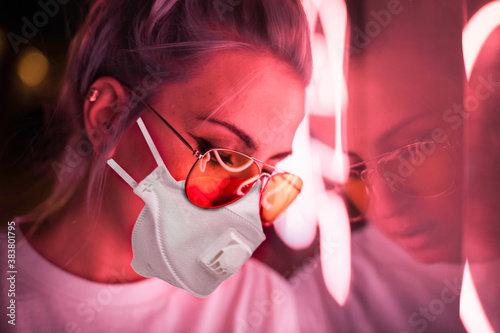 young woman with glasses and covid mask, at night colored lights photo