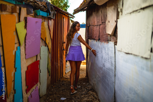 Female wearing a skirt paired with a white t-shirt and walking through an alley of old buildings © Wirestock Exclusives