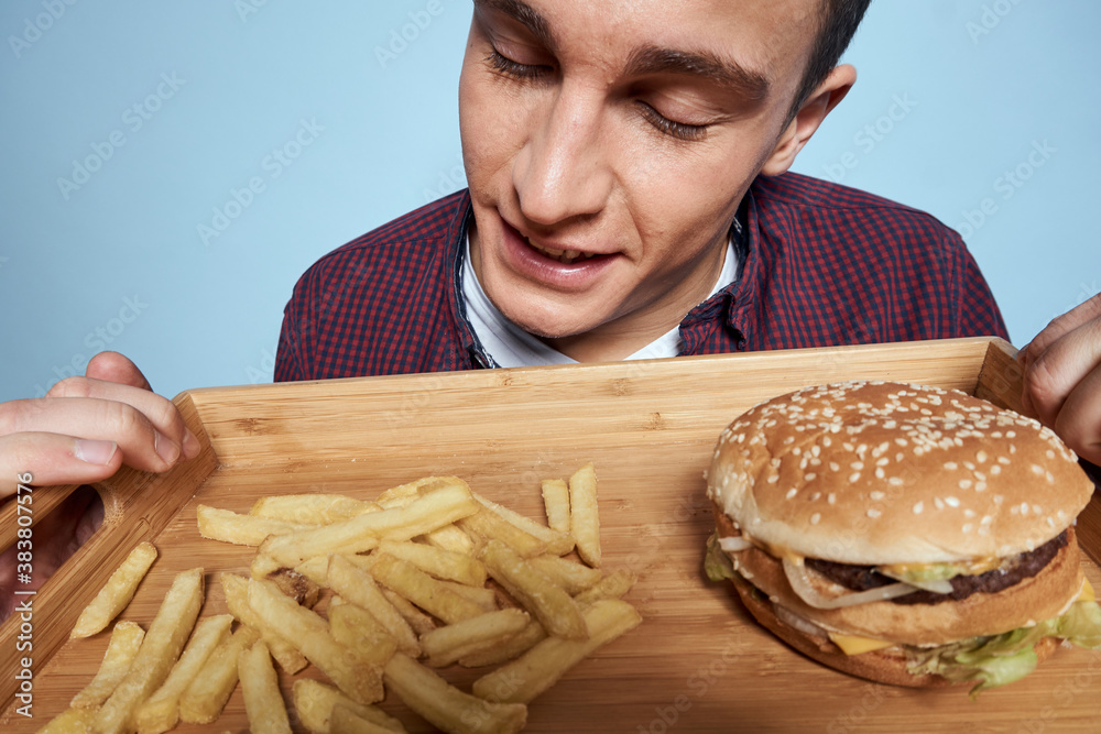 Man with wooden pallet fast food french fries hamburger hunger diet food blue background Man with wooden pallet fast food french fries hamburger hunger diet food blue background