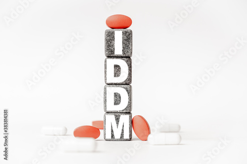 a group of white and red pills and cubes with the word IDDM Insulin-dependent diabetes mellitus on them, white background. Concept carehealth, treatment, therapy. photo