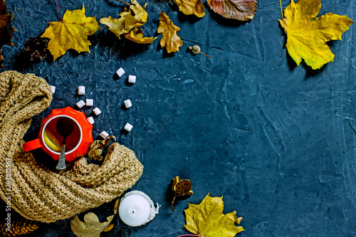 Autumn composition flat lay. Orange cup with hot drink and marshmallows surrounded by autumn dry maple and oak leaves, acorns, chestnuts, knitted scarf on a dark stone background, top view, copy space