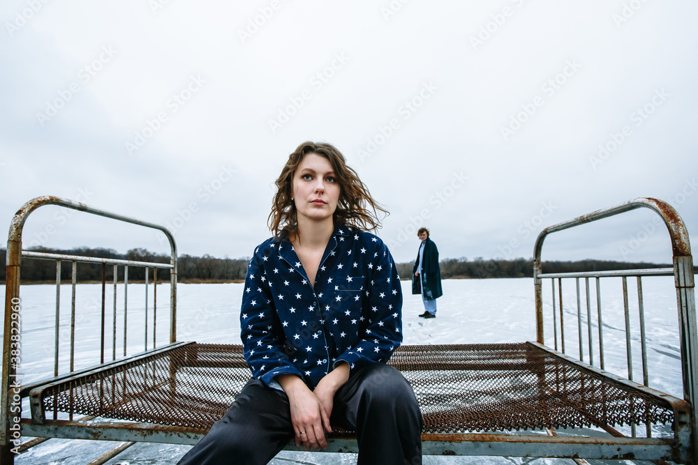 A guy and a girl in pajamas on the ice of a frozen lake. The girl is sitting on an iron bed, the guy next to her A guy and a girl in pajamas on the ice of a frozen lake. The girl is sitting on an iron bed, the guy next to her