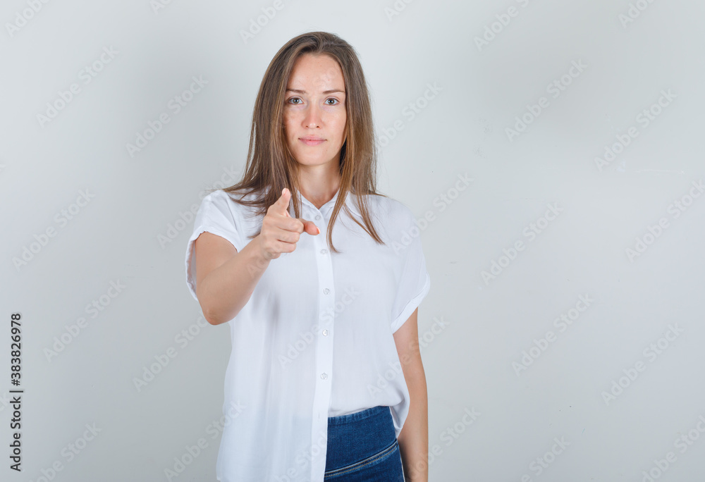 Young woman in white t-shirt, jeans pointing finger to camera and looking glad , front view.