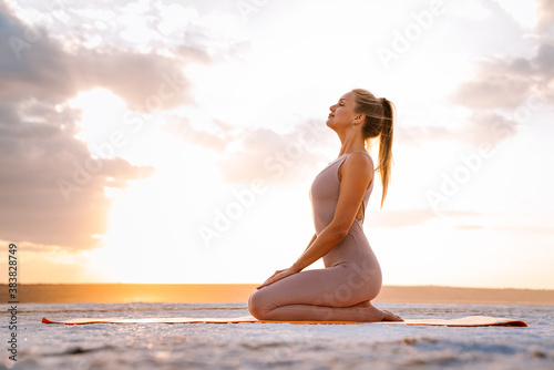 Young woman practicing yoga while doing workout on fitness mat outdoors