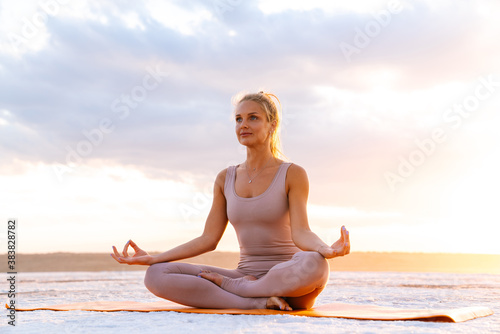 Young woman practicing yoga while doing workout on fitness mat outdoors