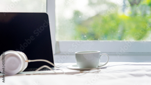 The laptop working on the white bed and coffee in the window on rainy day, Fresh morning holiday. Lifestyle Concept. soft and select focus.