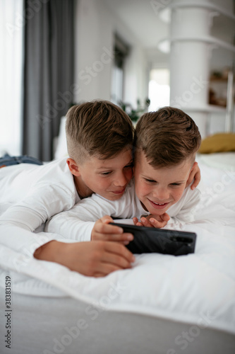 Two little brothers are playing games on the phone. Beautiful boys enjoying at home.