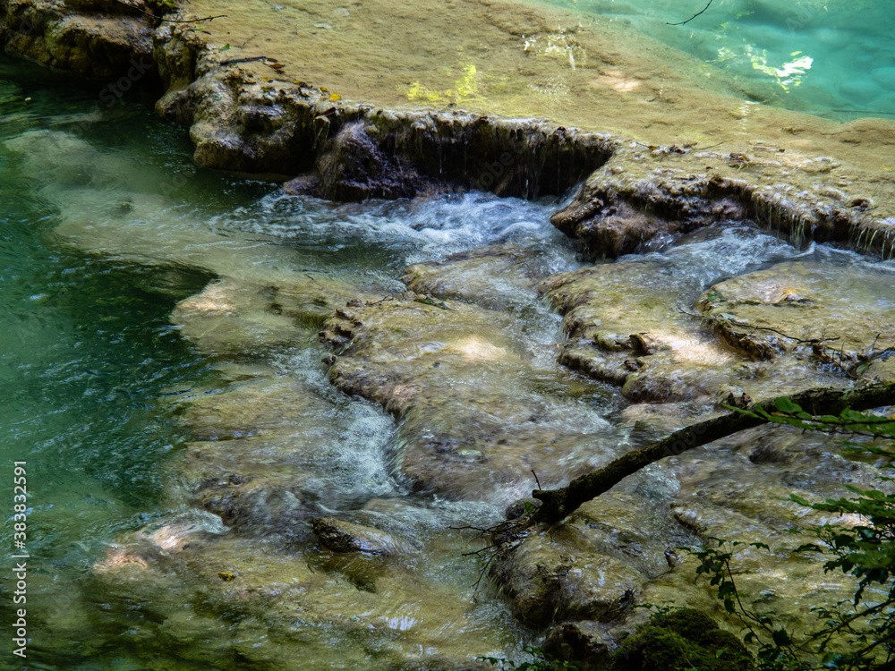 relaxing water stream with a green color, there is musk on the rocks and the water is a light turquoise color