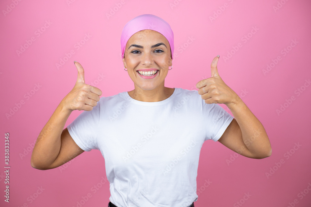Young beautiful woman wearing pink headscarf over isolated pink background smiling and doing the ok signal with her thumbs Young beautiful woman wearing pink headscarf over isolated pink background smiling and doing the ok signal with her thumbs