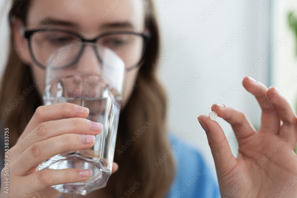 White pill being held by blonde woman while drinking water. Pandemic threat. Virus outbreak. White pill being held by blonde woman while drinking water. Pandemic threat. Virus outbreak.