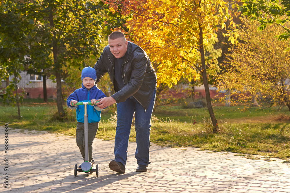 Obraz premium Dad teaches his two-year-old son to ride a scooter.