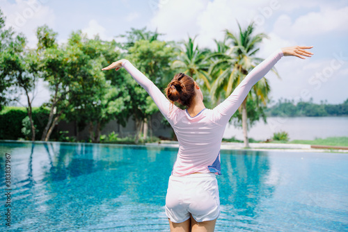 Asian woman traveler stretching arms up in the air at swimming pool.