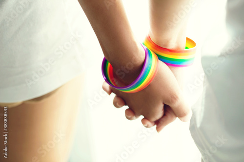 Closeup lesbian couple holding hands with a rainbow-patterned wristban on their wrists.Concept of LGBT, activism, community and freedom. photo