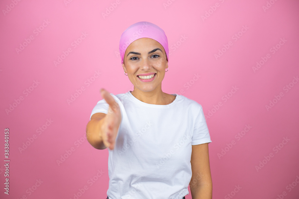 Young beautiful woman wearing pink headscarf over isolated pink background smiling friendly offering handshake as greeting and welcoming Young beautiful woman wearing pink headscarf over isolated pink background smiling friendly offering handshake as greeting and welcoming