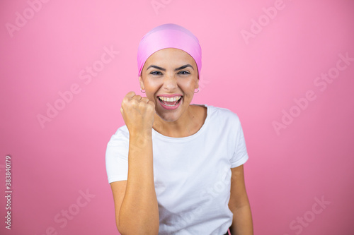 Young beautiful woman wearing pink headscarf over isolated pink background angry and mad raising fist frustrated and furious while shouting with anger. Rage and aggressive concept.