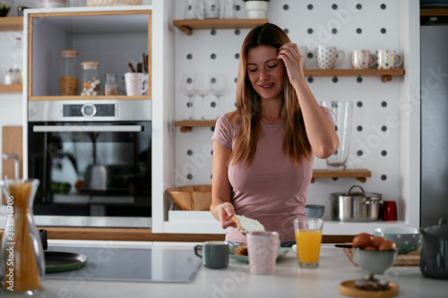 Young woman in kitchen. Beautiful woman preparing breakfast and drinking coffee..