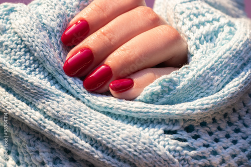 Female hand in a blue knitted sweater fabric with beautiful glossy manicure - burgundy, dark red color nails. Selective focus. Closeup view