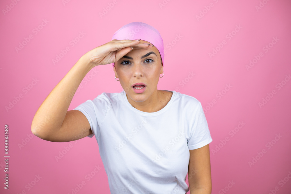 Young beautiful woman wearing pink headscarf over isolated pink background very happy and smiling looking far away with hand over head. searching concept.