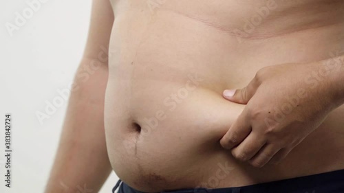 Wallpaper Mural Close up of a big male stomach. The fat man checks his waist by left hand, he is obese and overweight isolated on white background. 4K Resolution. Torontodigital.ca