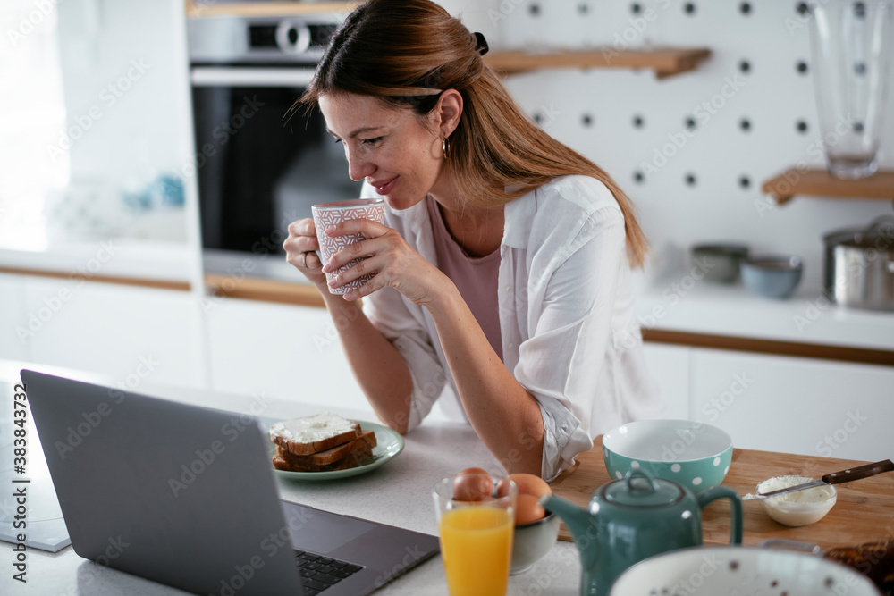 Beautiful woman eating breakfast in the kitchen. Young woman reading the news online.. Beautiful woman eating breakfast in the kitchen. Young woman reading the news online..