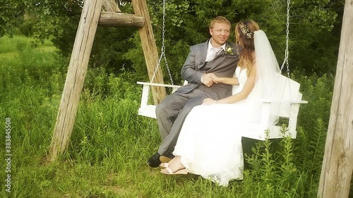 A bride and groom shaking hands while sitting on a white bench swing