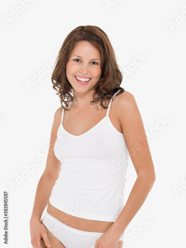 Portrait of a young smiling woman in camisole and knickers against white background