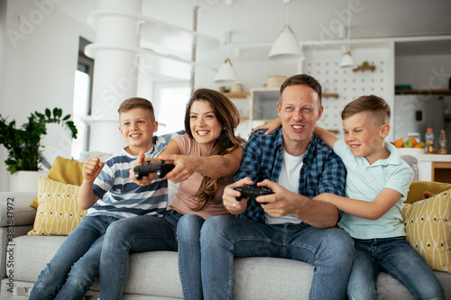 Husband and wife playing video games with joysticks in living room. Loving couple are playing video games with kids at home..