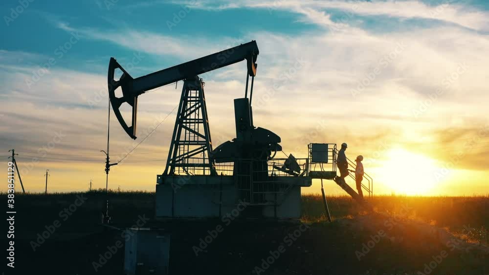 Oil pumping constructions and two technicians at sunset
