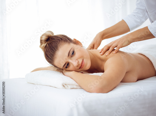 Young and blonde woman enjoying massage of back in spa salon. Beauty concept