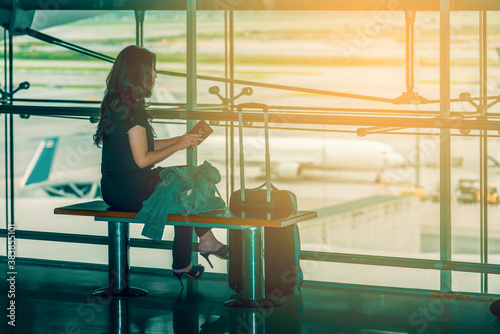 Asian woman at international airport, checking passport, luggage and waiting for her flight and background blur airplane, view from airport terminal. (vintage color tone, lens blur effect)