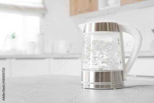 Modern glass electric kettle boiling on kitchen table photo