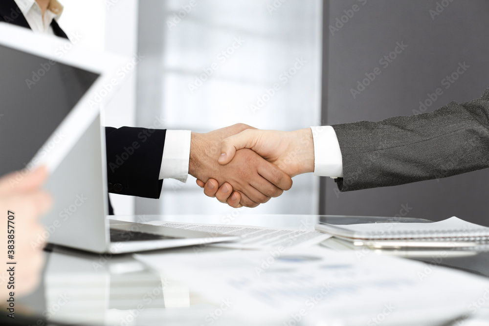 Unknown diverse business people are shaking hands finishing up meeting at the desk in office, close-up. Handshake concept