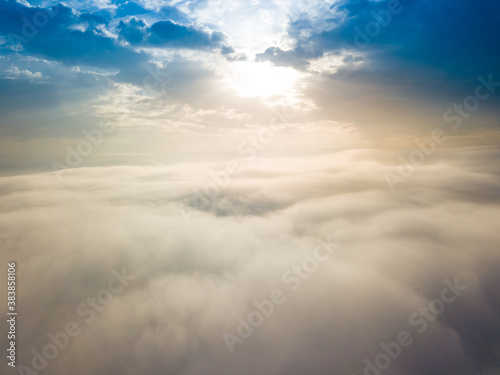 Aerial drone flight over the fog. There are thick clouds of fog below, the sun breaks through the clouds.