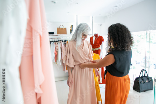 Valokuva Black haired shop assistant helping woman to try on new dress and adjusting waistband