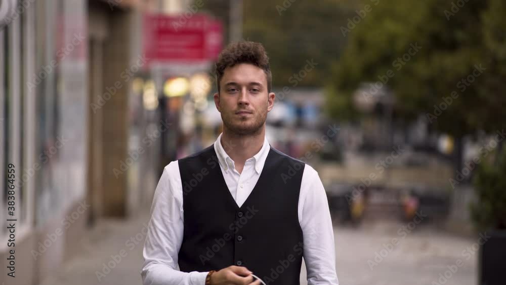 An elegant young guy wearing a black waistcoat, a white shirt and a simple green protective Covid-19 facemask, slowly removing it with his right hand and looking directly into the camera, static 4k. An elegant young guy wearing a black waistcoat, a white shirt and a simple green protective Covid-19 facemask, slowly removing it with his right hand and looking directly into the camera, static 4k.