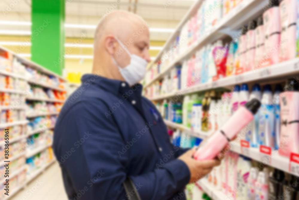 A masked man in a supermarket chooses a cleaning product. Coronavirus pandemic. Blurred.