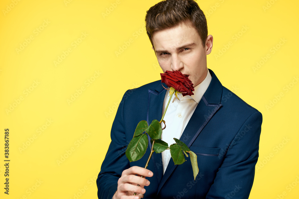 Young man in a classic suit with a red rose in his hand on a yellow background emotions cropped view model Young man in a classic suit with a red rose in his hand on a yellow background emotions cropped view model