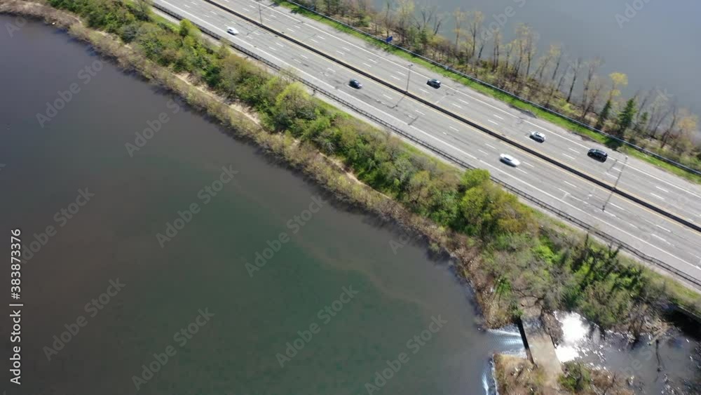 An aerial view of reflective lakes during the day. The camera is tilted down, pan sharp left then dolly in over one of the lakes. The parkway below has some automobile traffic which is light and easy. An aerial view of reflective lakes during the day. The camera is tilted down, pan sharp left then dolly in over one of the lakes. The parkway below has some automobile traffic which is light and easy.